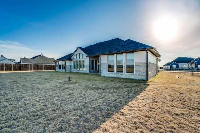 back of house featuring a yard, stone siding, and fence