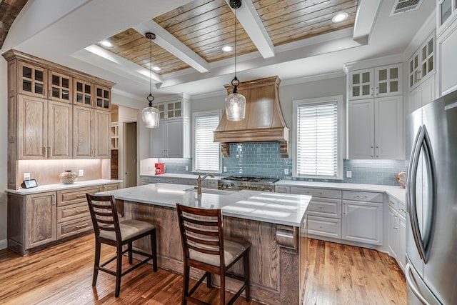 kitchen with glass insert cabinets, freestanding refrigerator, light countertops, and an island with sink