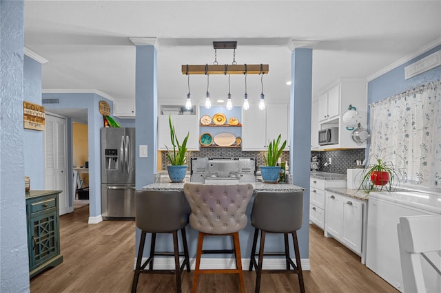 kitchen featuring a center island, pendant lighting, stainless steel appliances, white cabinets, and light stone countertops