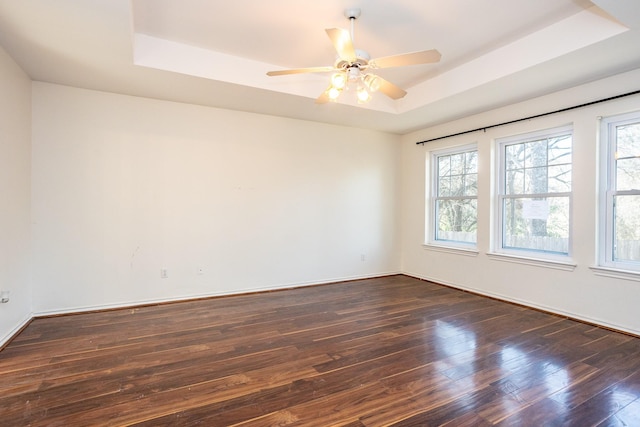 unfurnished room featuring dark wood-style floors, a tray ceiling, ceiling fan, and baseboards