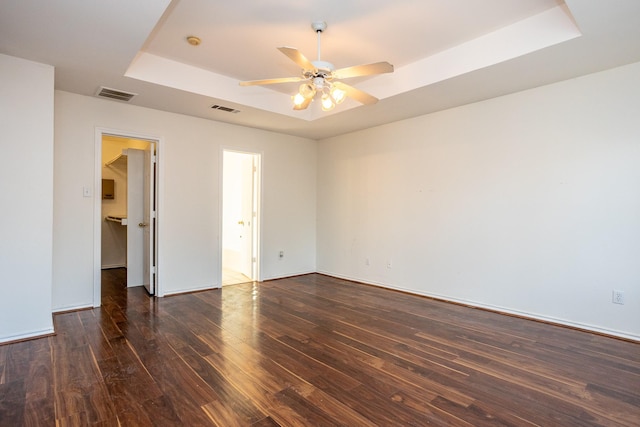 spare room featuring a tray ceiling, dark wood-style flooring, visible vents, and a ceiling fan