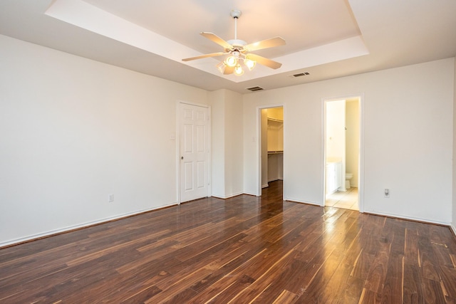 unfurnished bedroom with dark wood finished floors, a closet, a raised ceiling, visible vents, and a spacious closet