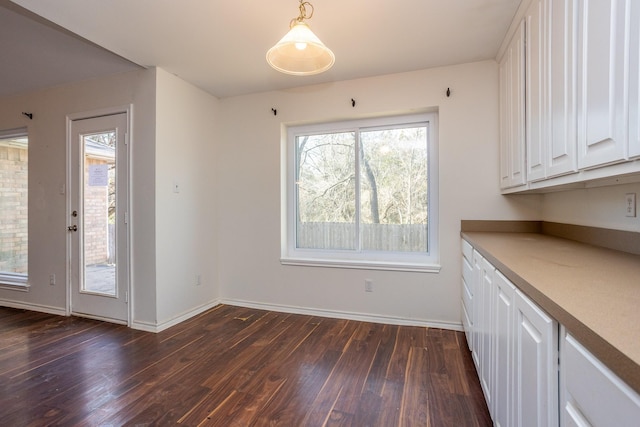 unfurnished dining area featuring baseboards and dark wood-type flooring