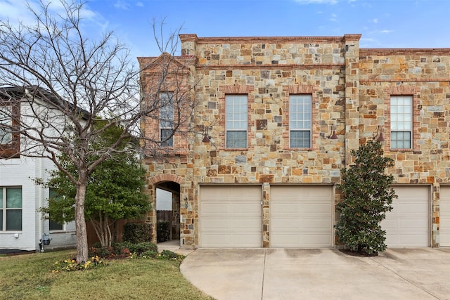 multi unit property featuring an attached garage, stone siding, and concrete driveway