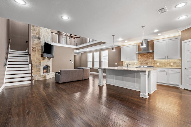 kitchen featuring decorative light fixtures, open floor plan, a kitchen island with sink, white cabinets, and wall chimney exhaust hood