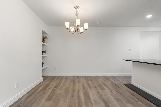 unfurnished dining area with baseboards, light wood-style floors, built in shelves, and an inviting chandelier