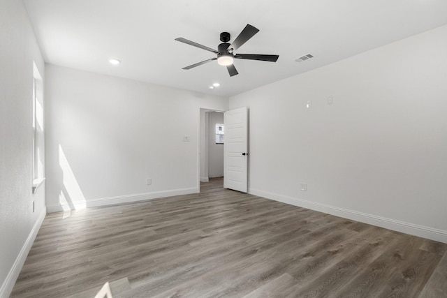 empty room featuring dark wood finished floors, a wealth of natural light, visible vents, a ceiling fan, and baseboards