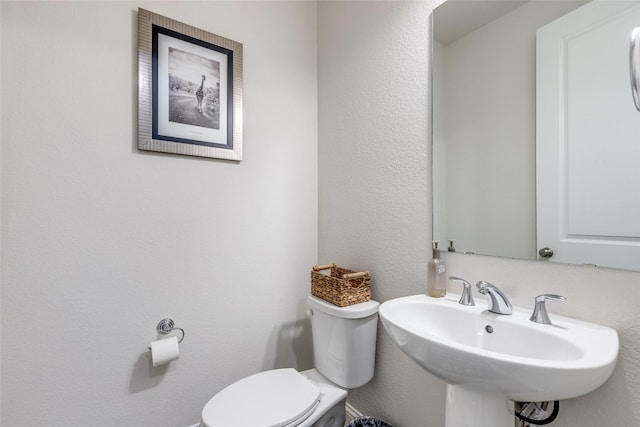 half bathroom with a textured wall, a sink, and toilet