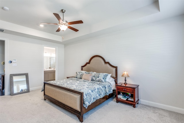 bedroom featuring light colored carpet, visible vents, baseboards, a tray ceiling, and ensuite bath