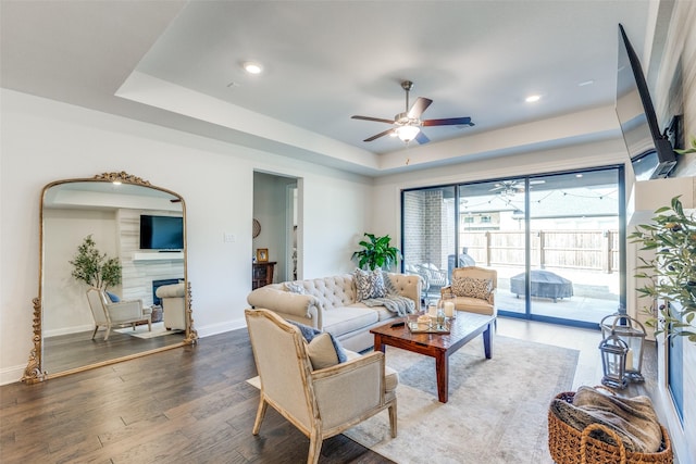 living area featuring wood finished floors, a fireplace, a raised ceiling, and baseboards