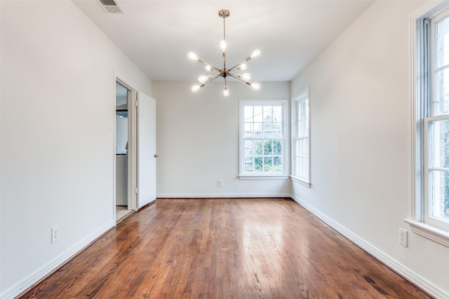 spare room with baseboards, wood finished floors, a notable chandelier, and visible vents