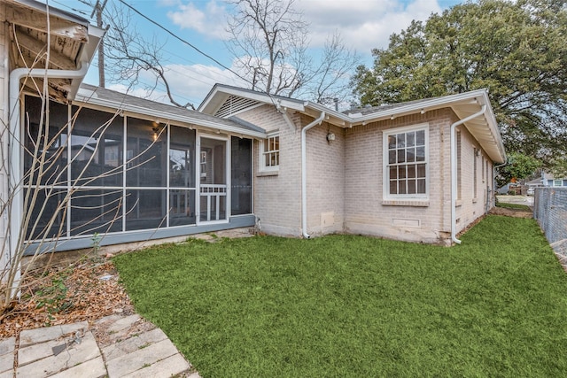 rear view of property with fence, brick siding, a sunroom, and a lawn