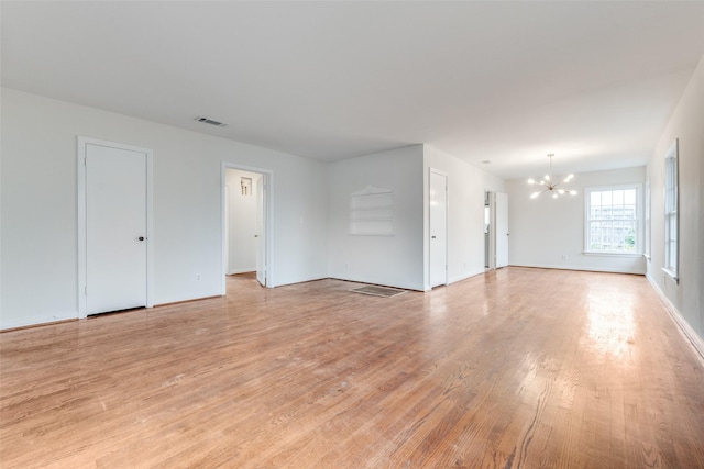 unfurnished living room featuring a notable chandelier, baseboards, visible vents, and light wood-style flooring