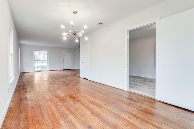 spare room with light wood finished floors, visible vents, baseboards, and an inviting chandelier