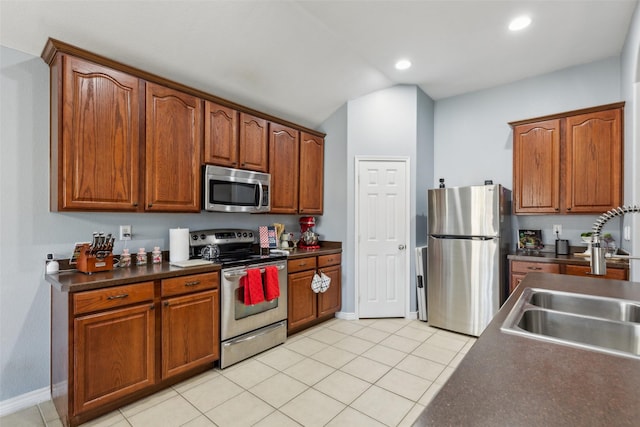 kitchen featuring stainless steel appliances, dark countertops, light tile patterned flooring, vaulted ceiling, and a sink