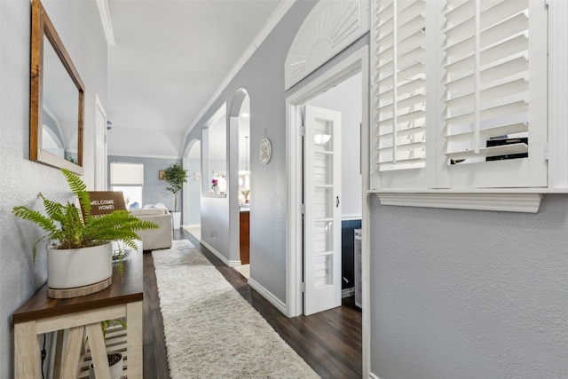 hall with arched walkways, a textured wall, dark wood finished floors, and crown molding