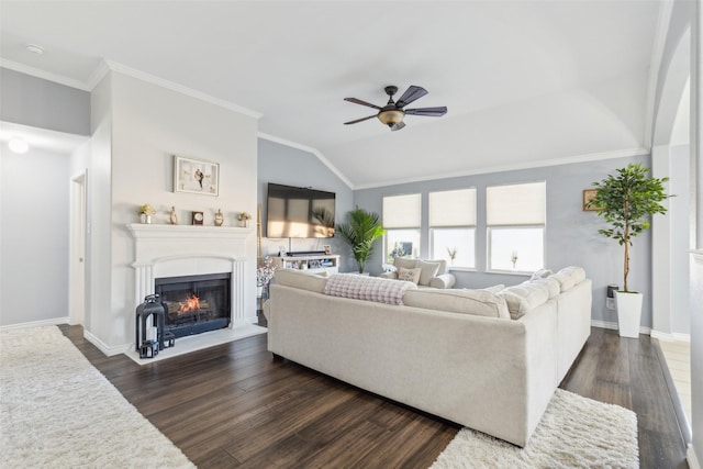 living area with a warm lit fireplace, baseboards, dark wood finished floors, ornamental molding, and vaulted ceiling