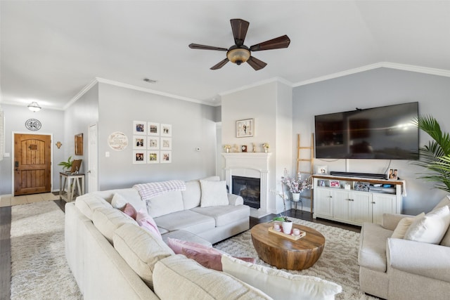 living area with visible vents, a ceiling fan, a fireplace with flush hearth, ornamental molding, and vaulted ceiling