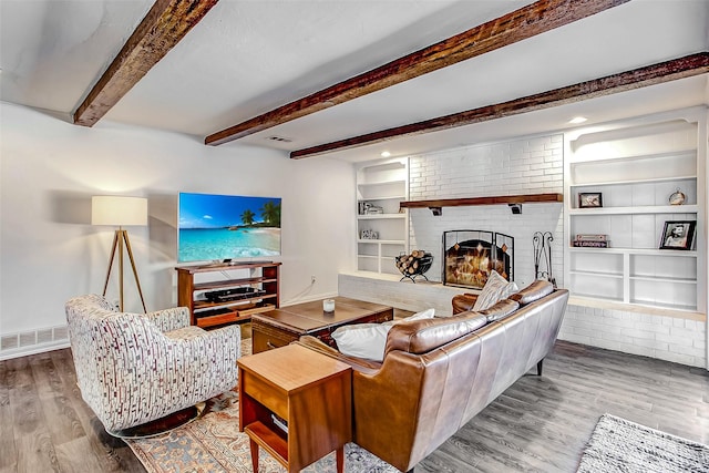 living room featuring built in features, a fireplace, visible vents, wood finished floors, and baseboards