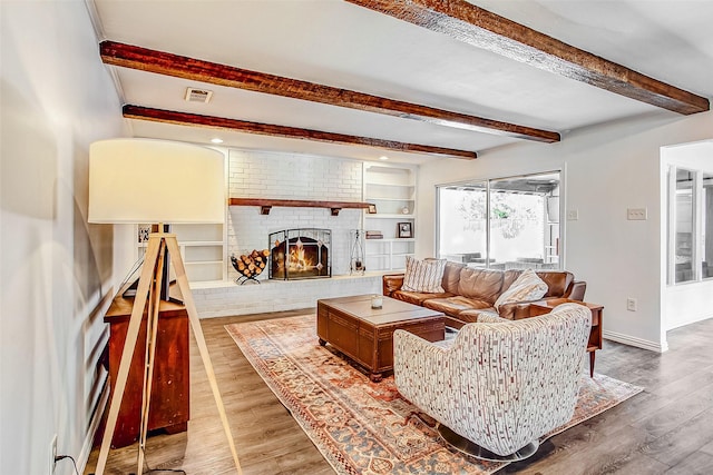 living area with beamed ceiling, light wood-type flooring, visible vents, and a brick fireplace