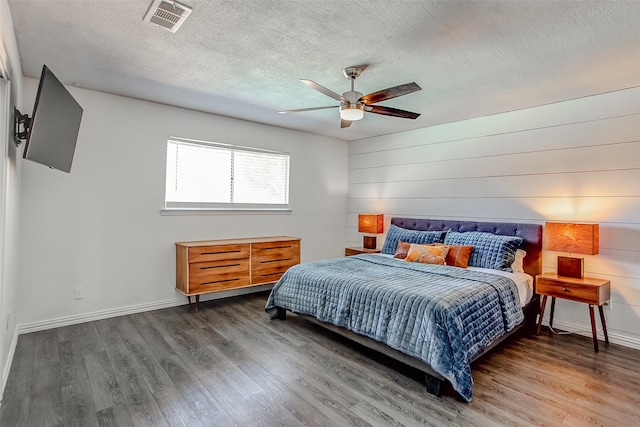 bedroom featuring a textured ceiling, a ceiling fan, visible vents, baseboards, and dark wood finished floors