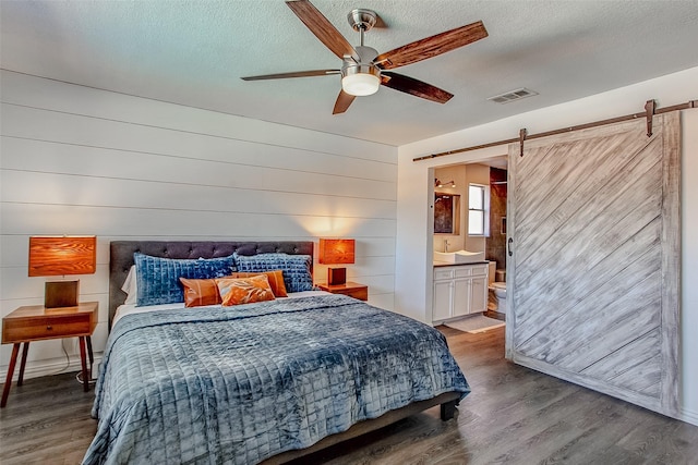 bedroom featuring a barn door, a textured ceiling, visible vents, and wood finished floors