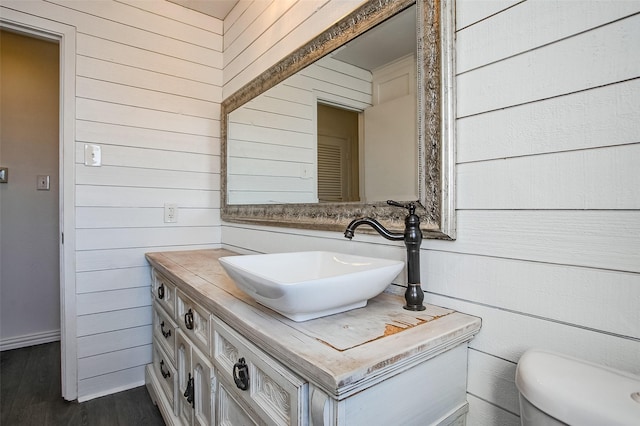 bathroom featuring wood walls, vanity, toilet, and wood finished floors