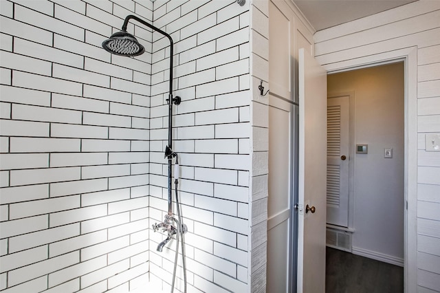 bathroom with tiled shower, visible vents, and baseboards