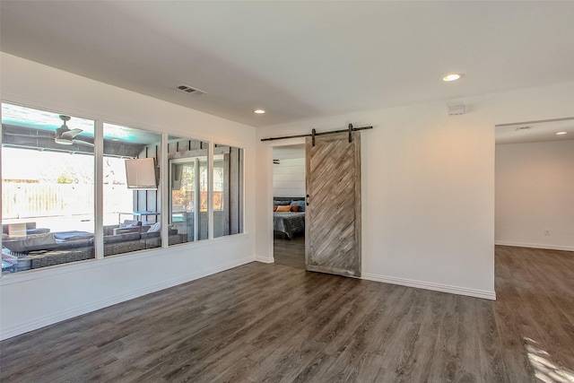 empty room with dark wood finished floors, recessed lighting, visible vents, a barn door, and baseboards