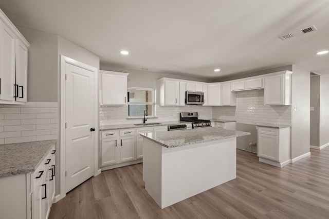 kitchen featuring light stone counters, visible vents, light wood-style flooring, appliances with stainless steel finishes, and a sink