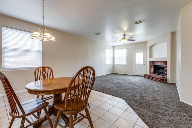 dining space with light tile patterned floors, visible vents, a brick fireplace, light carpet, and ceiling fan with notable chandelier