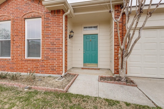 view of exterior entry with a garage and brick siding