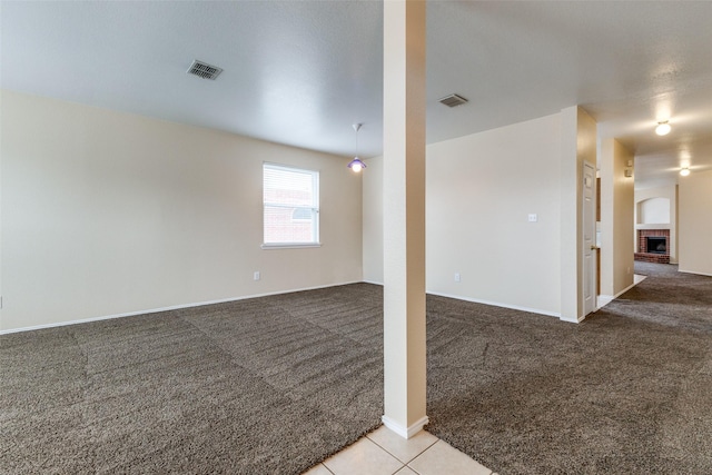 carpeted empty room featuring a brick fireplace, tile patterned flooring, visible vents, and baseboards