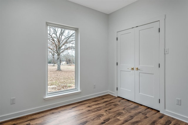 unfurnished bedroom with dark wood-style floors, baseboards, and a closet