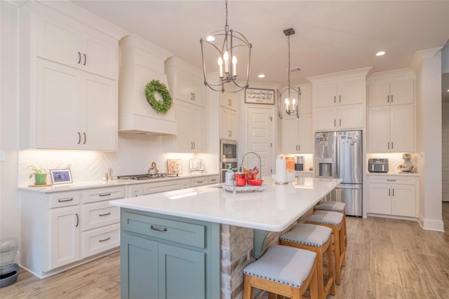 kitchen with a kitchen breakfast bar, a kitchen island with sink, stainless steel appliances, light countertops, and white cabinetry