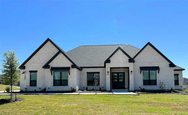 view of front of home with brick siding, a front lawn, and roof with shingles