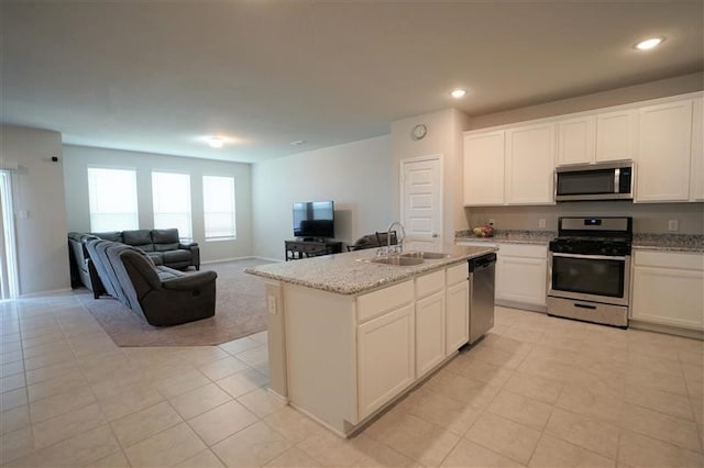 kitchen with an island with sink, appliances with stainless steel finishes, open floor plan, white cabinetry, and a sink