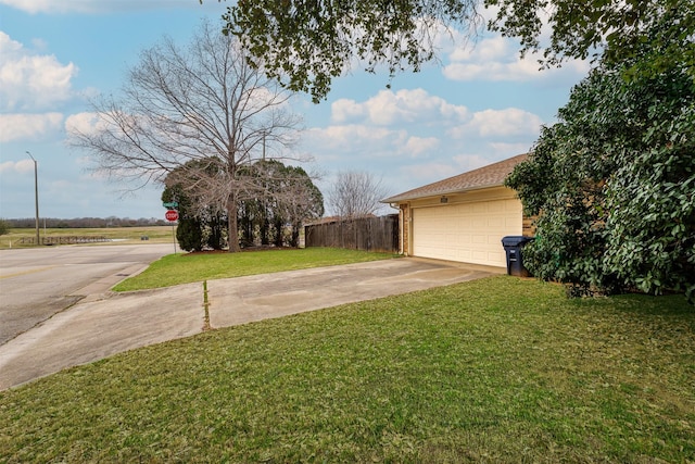 view of yard featuring a garage, concrete driveway, and fence