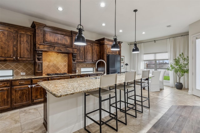 8 Center Ct, Heath, TX 75032 - kitchen featuring freestanding refrigerator, a kitchen island with sink, light stone counters, dark brown cabinetry, and recessed lighting