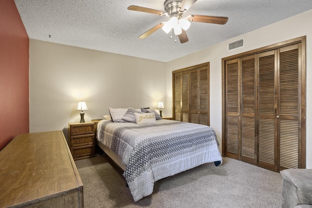 bedroom featuring dark colored carpet, visible vents, a textured ceiling, and two closets