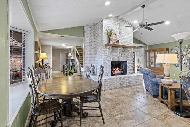 dining space featuring vaulted ceiling with beams, ceiling fan, a fireplace, and stairway