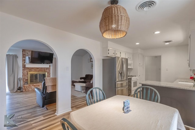 dining room with light wood-style floors, a fireplace, visible vents, and recessed lighting