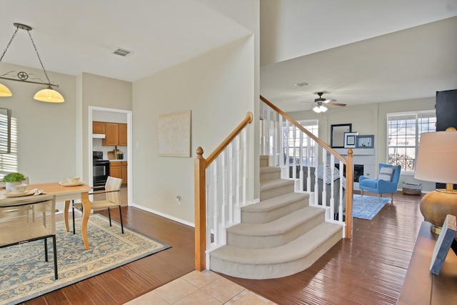 staircase featuring baseboards, visible vents, ceiling fan, wood finished floors, and a fireplace