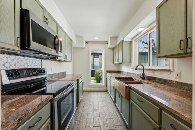 kitchen with a sink, baseboards, appliances with stainless steel finishes, dark stone countertops, and green cabinetry