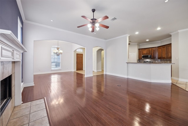 unfurnished living room with ceiling fan with notable chandelier, a fireplace, baseboards, and wood finished floors