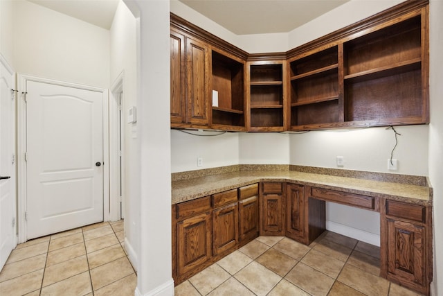 kitchen with light tile patterned floors, light stone counters, baseboards, open shelves, and built in desk