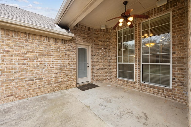 view of exterior entry featuring a patio, brick siding, roof with shingles, and a ceiling fan