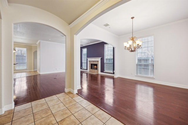 unfurnished living room featuring baseboards, visible vents, a premium fireplace, light wood-type flooring, and a notable chandelier