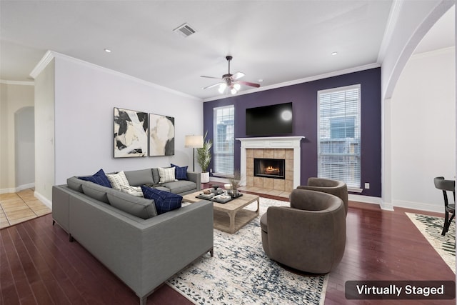 living area with plenty of natural light, visible vents, arched walkways, a tiled fireplace, and wood finished floors