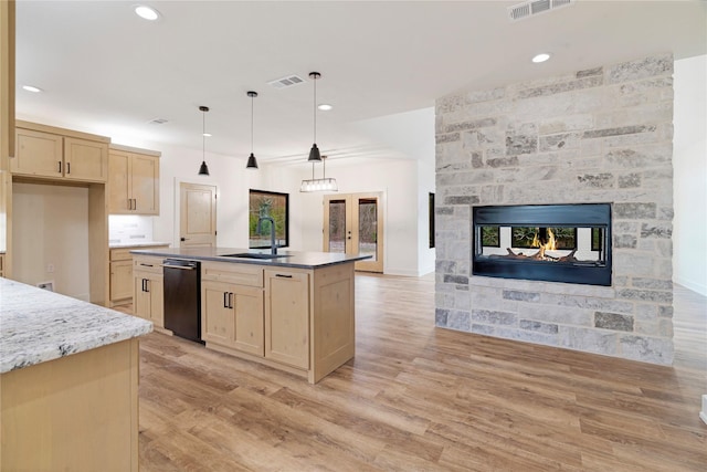 kitchen with visible vents, hanging light fixtures, a kitchen island with sink, light brown cabinets, and a sink